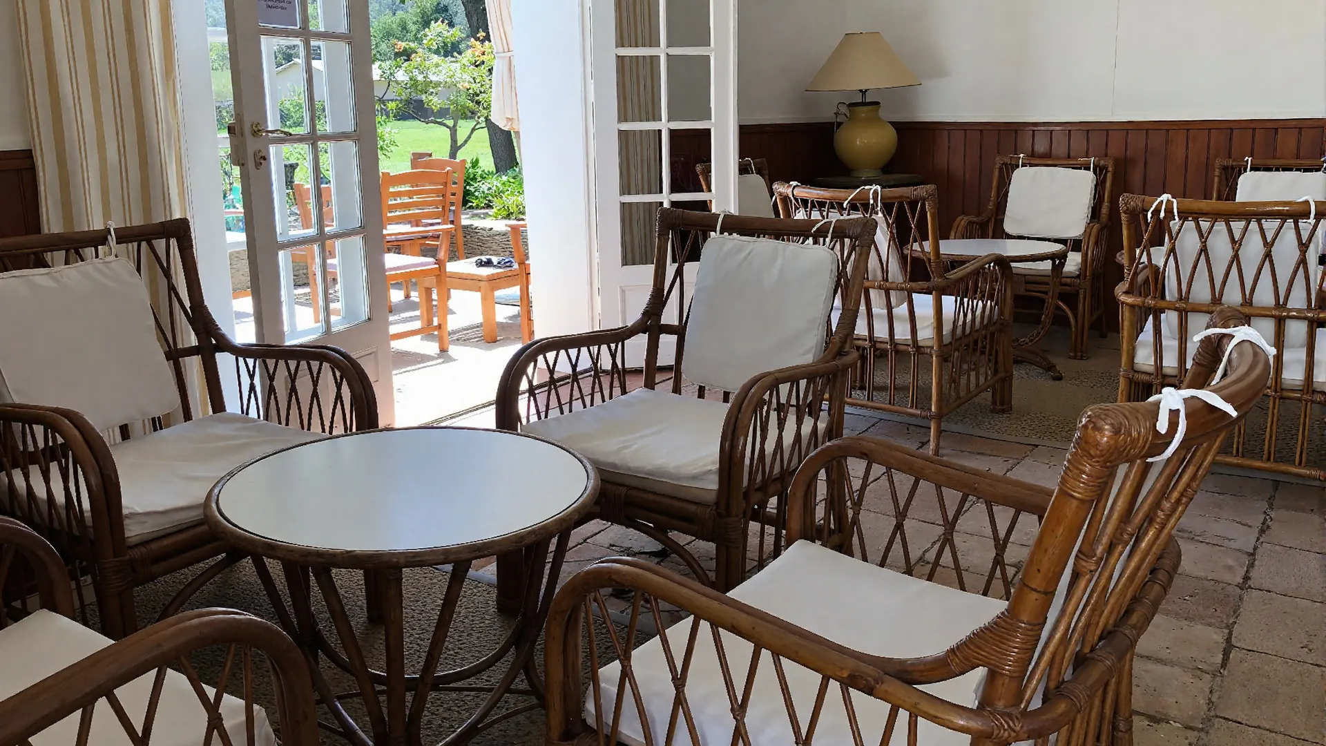 Salon en rotin du bar du Manoir, ouvert sur le jardin par des portes-fenêtres